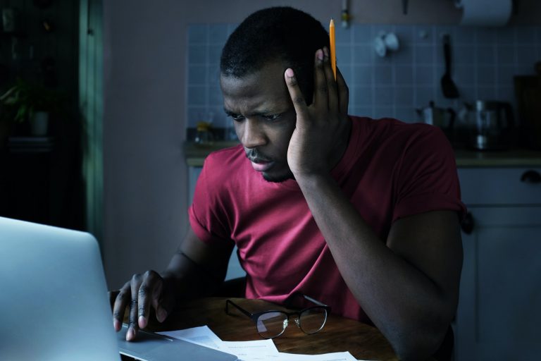 Young african american man sits at home in front of laptop trying to check some data