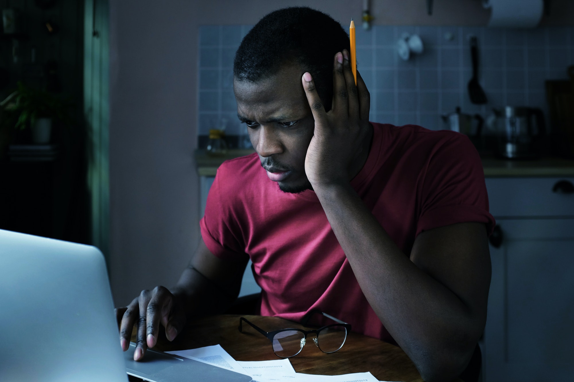 Young african american man sits at home in front of laptop trying to check some data